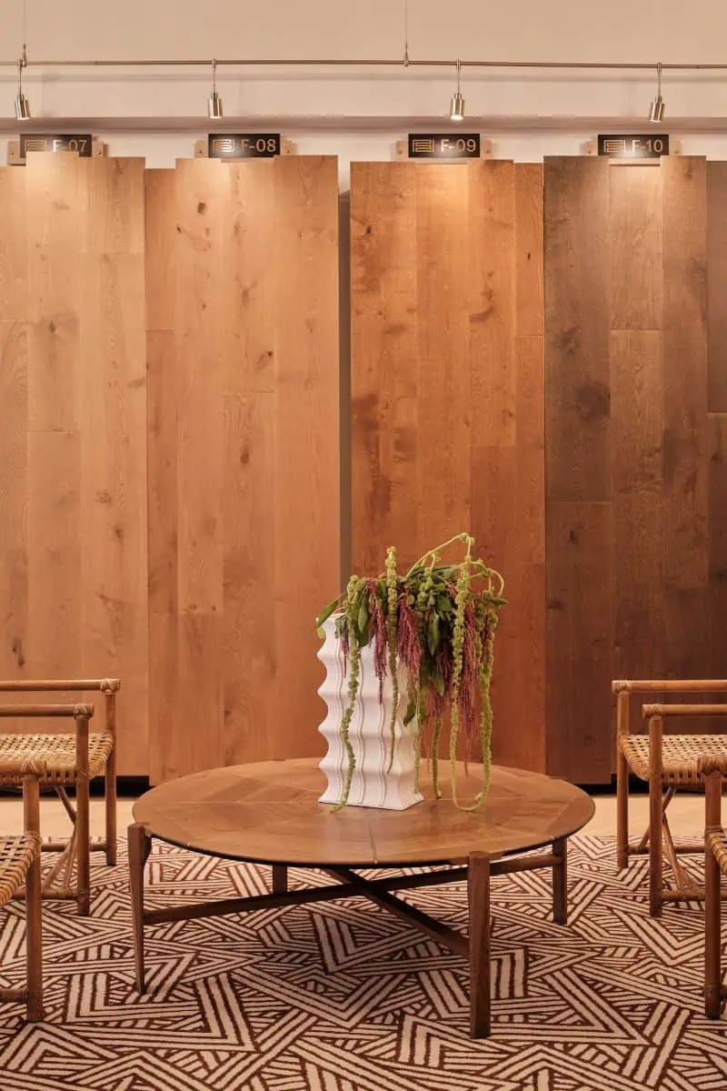 A cozy room features a round wooden table with a wavy vase, surrounded by chairs, and wooden panels displayed behind.