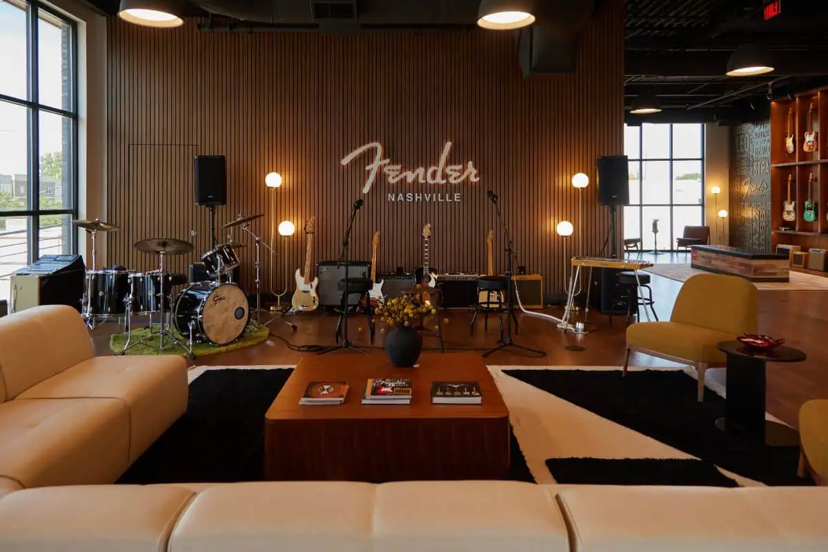 Music-themed lounge with drum kit, guitars, and microphones. "Fender Nashville" sign on wood-paneled wall. Cozy seating and decorative books complete the space.