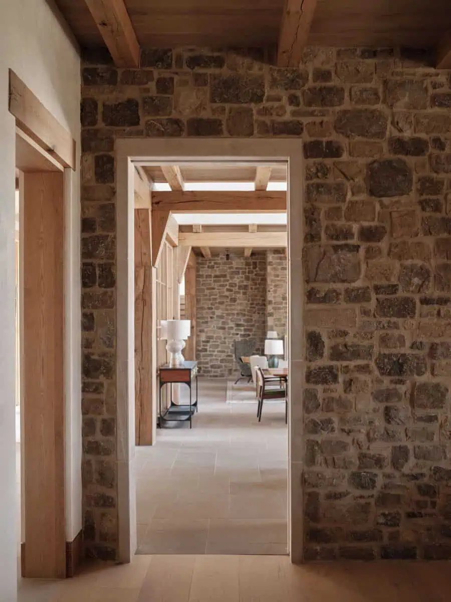 A rustic interior features stone walls, wooden beams, and a cozy dining area with lamps and chairs, creating a warm ambiance.