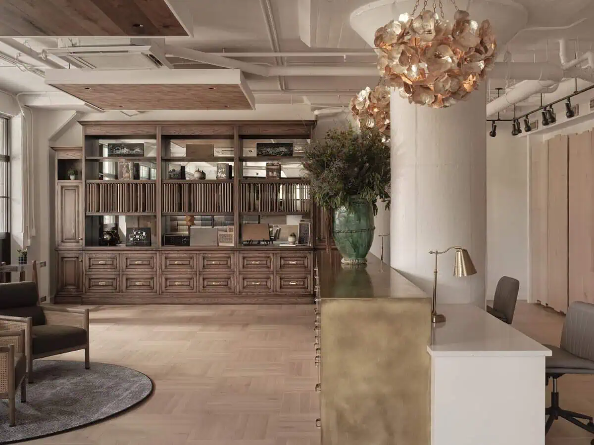 Elegant room with wooden bookshelves, a brass-accented desk, and floral chandeliers, creating a sophisticated atmosphere. Large windows provide natural light.