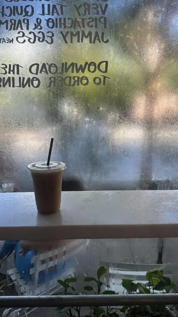 Iced coffee by foggy window with sign reflection.