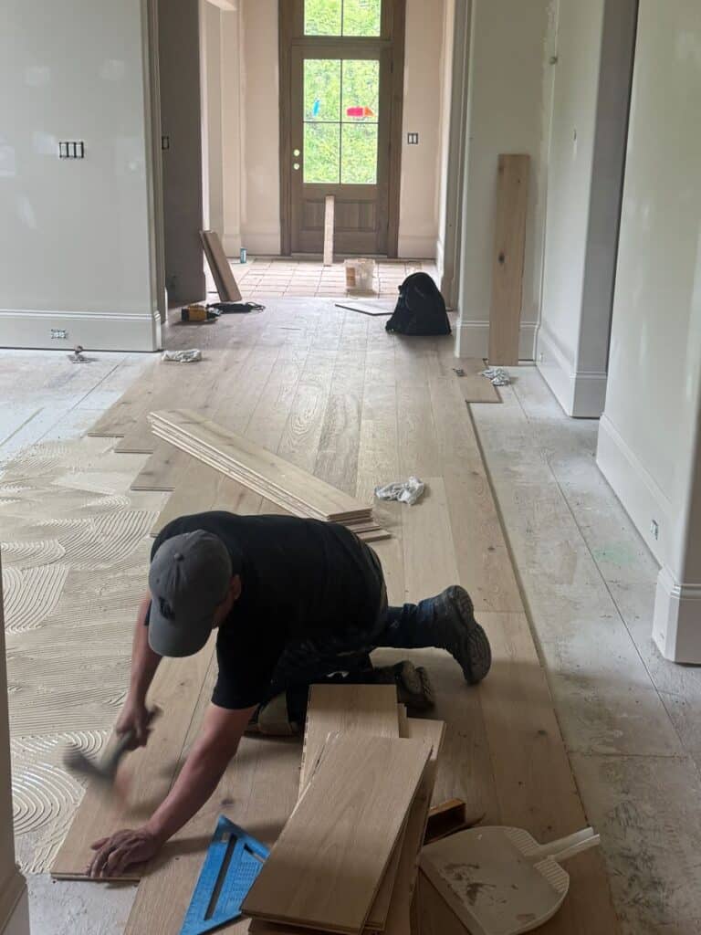 Worker installing hardwood flooring in hallway.