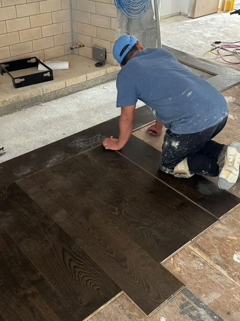 Worker installing dark wood flooring indoors.